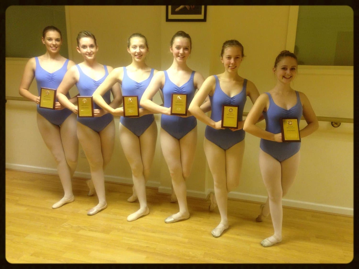 Ballet students holding award plaques beside the barre